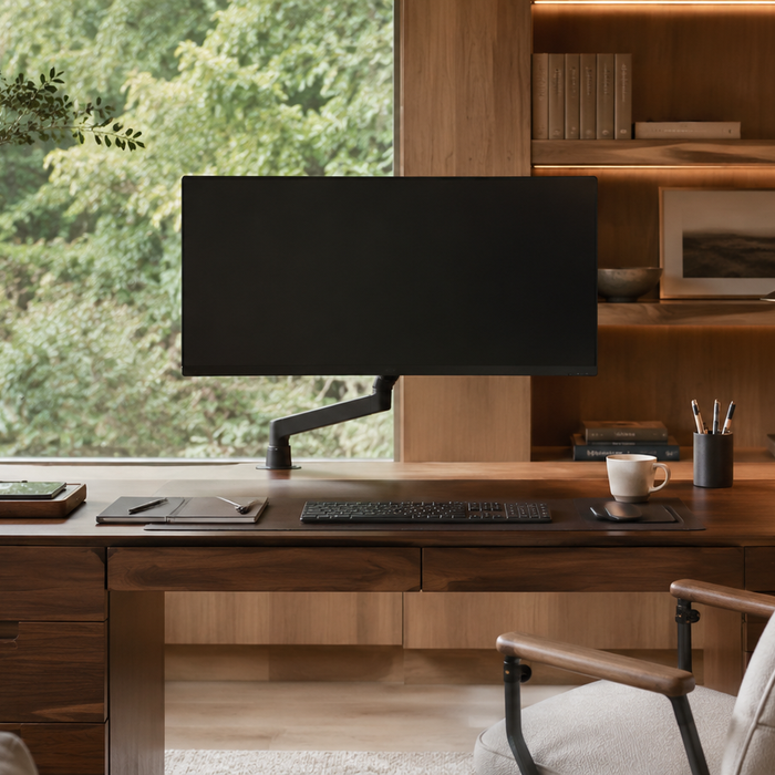 Single monitor on a low-profile monitor arm above a long wooden desk in a warm home office