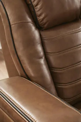 Close-up of Ashley Gruaro Power Reclining Loveseat (PCU1420018) seat upholstery, highlighting its plush back cushioning, horizontal channel stitching, supportive side bolsters, and contrasting dark piping.