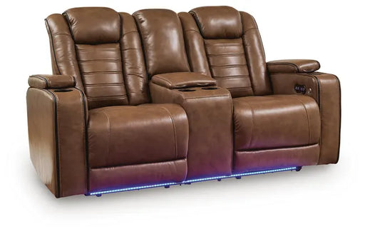 Three-quarter front view of Ashley Gruaro Brown Power Reclining Loveseat (PCU1420018), featuring padded backrests, closed footrests, center console with cup holders, and blue LED base lighting.