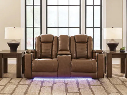 Ashley Gruaro Brown Power Reclining Loveseat (PCU1420018) displayed in an elegant living room with padded seating, center console, matching end tables, and blue LED base lighting.