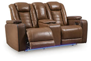 Ashley Gruaro Brown Power Reclining Loveseat (PCU1420018) with dual extended footrests, padded headrests, center console with cup holders, and blue LED underlighting.