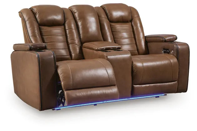 Ashley Gruaro Brown Power Reclining Loveseat (PCU1420018) with dual extended footrests, padded headrests, center console with cup holders, and blue LED underlighting.