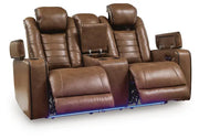 Ashley Gruaro Brown Power Reclining Loveseat (PCU1420018) with extended footrests, open storage compartments, center console, cup holders, and blue LED base lighting.