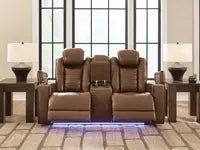 Ashley Gruaro Power Reclining Loveseat (PCU1420018) in a contemporary living room, featuring two plush reclining seats, a center storage console, cup holders, and blue LED floor lighting.