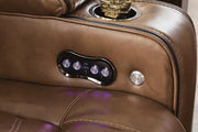Close-up of Ashley Gruaro Brown Power Reclining Loveseat (PCU1420018), highlighting illuminated power recline controls, USB charging ports, built-in cup holder, and brown upholstery with contrast stitching.
